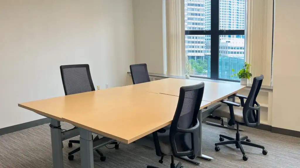 Bright four-desk office in Boston with ergonomic chairs and large window overlooking city buildings.