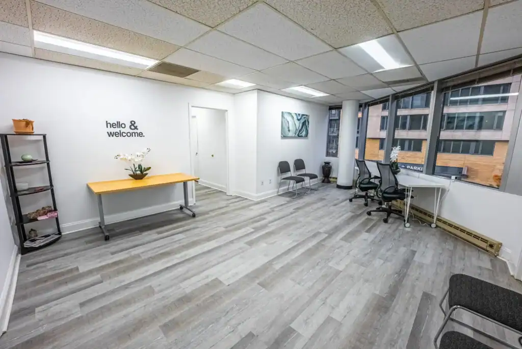 Bright office lounge with “hello & welcome” sign, seating, and large windows overlooking neighboring buildings.