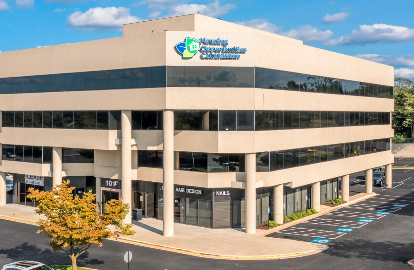 Modern multi-story office building in Gaithersburg MD with large tinted windows, columns, accessible parking, and signage for Housing Opportunities Commission