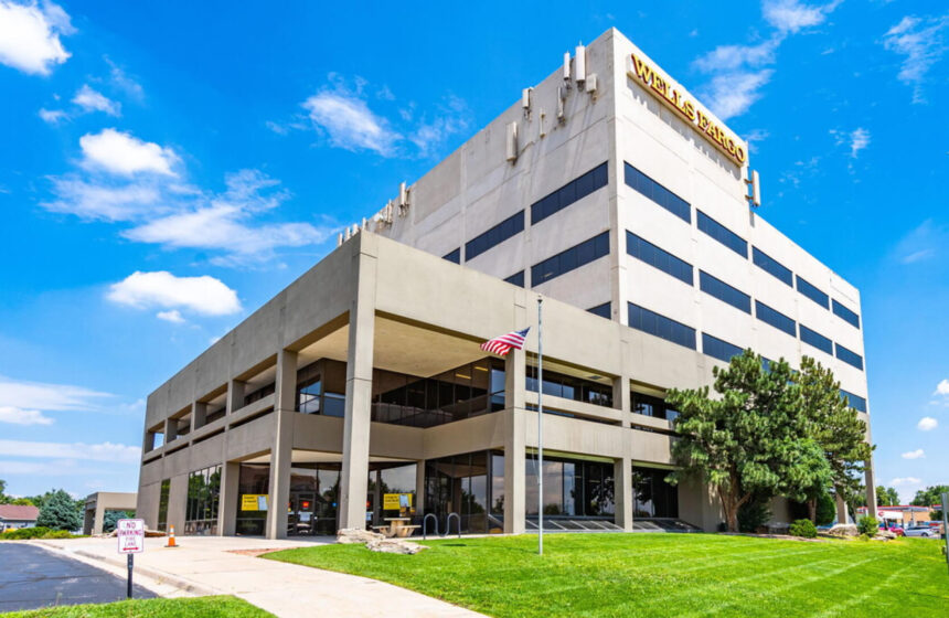 A modern office building in Denver CO with the Wells Fargo logo, American flag in front, and green lawn under a blue sky.