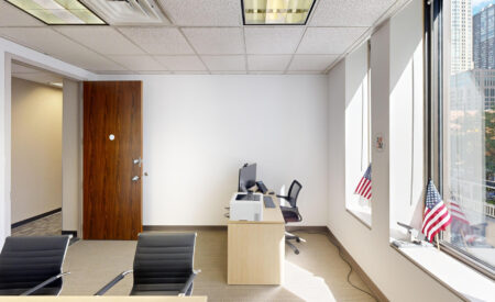 Office in Chicago with wood desk, computer setup, black chairs, and large windows with American flags